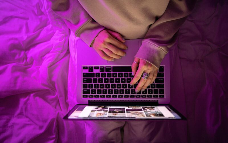 Top view of unrecognizable person using laptop with neon purple lighting, creating a vibrant high-tech atmosphere.